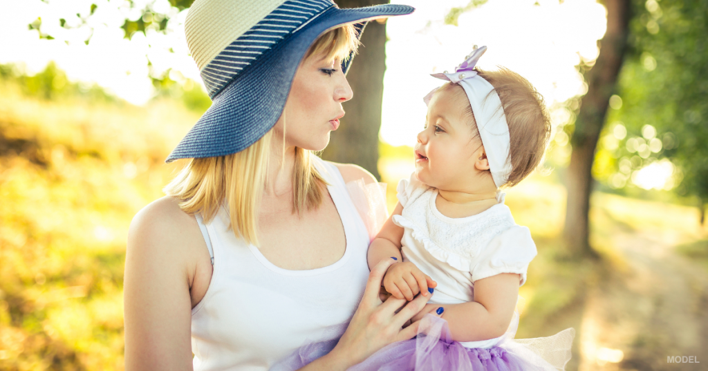 Blonde young woman in blue floppy hat holding baby girl looking at each other