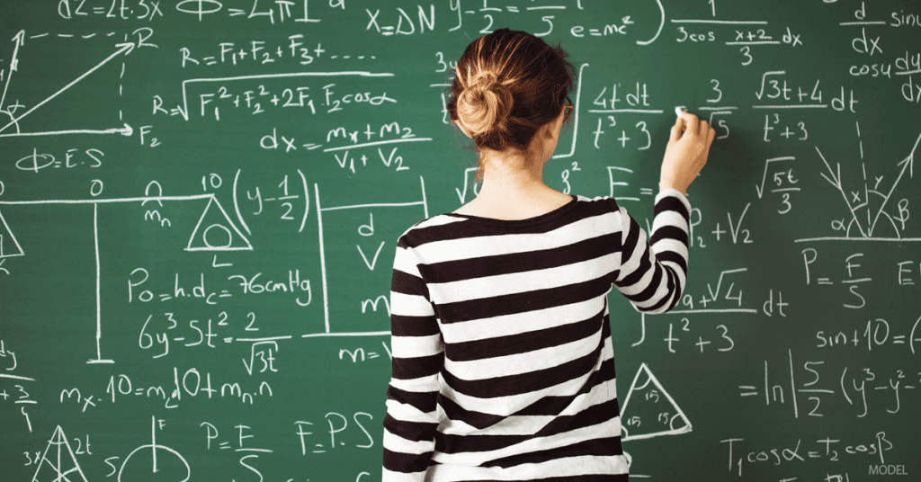 Woman wearing black and white striped shirt doing math calculations on a chalk board