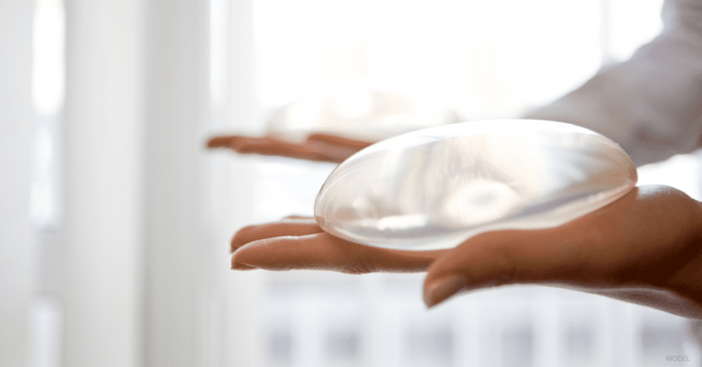 Closeup of outstretched hand holding a breast implant in the palm