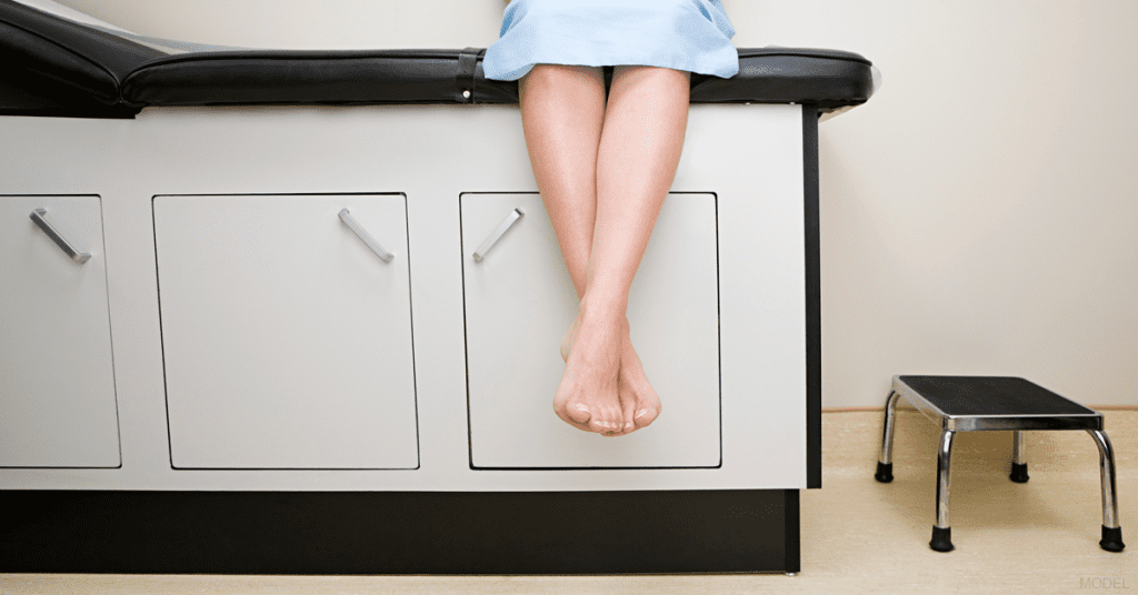 Lower body of woman blue surgical gown sitting in examination room