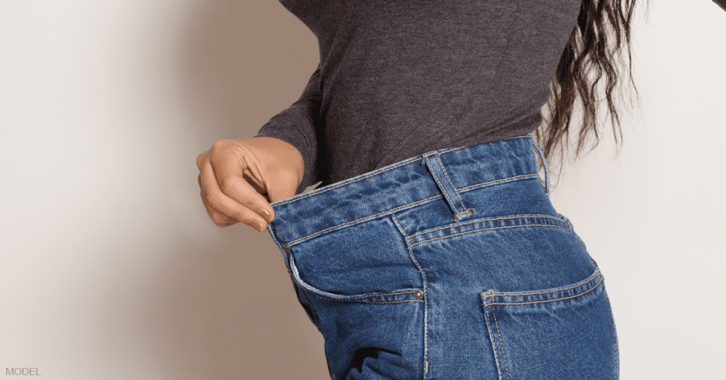 Side view of a woman holding out the loose waist of blue jeans