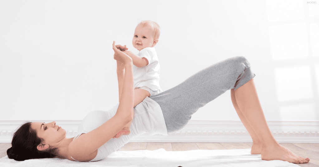 A woman plays with her baby while thinking about the best time to get a tummy tuck procedure.