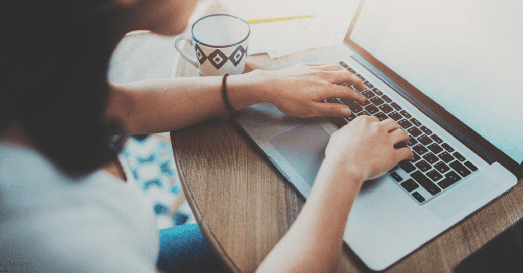 Woman's hands on laptop keyboard with coffee next to it