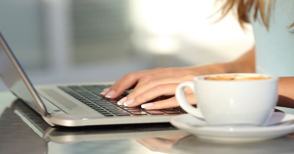 Woman's hands on laptop keyboard with cappuccino to the side