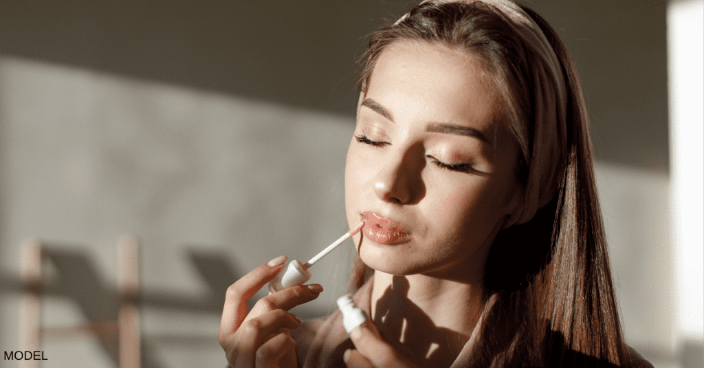 Woman with eyes closed putting on lipgloss. (MODEL)