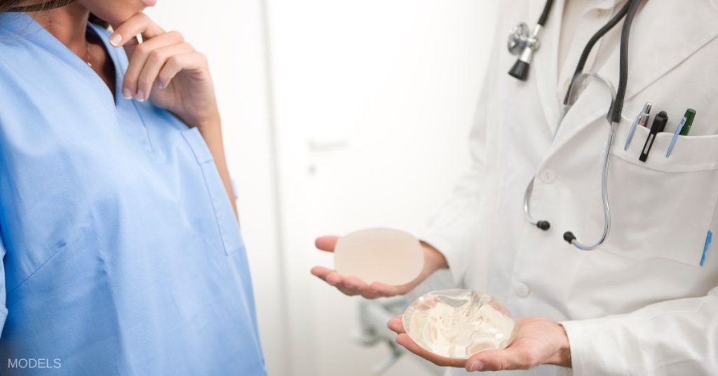 Doctor holding two types of implants in front of a woman with a hand to her chin. (MODELS)