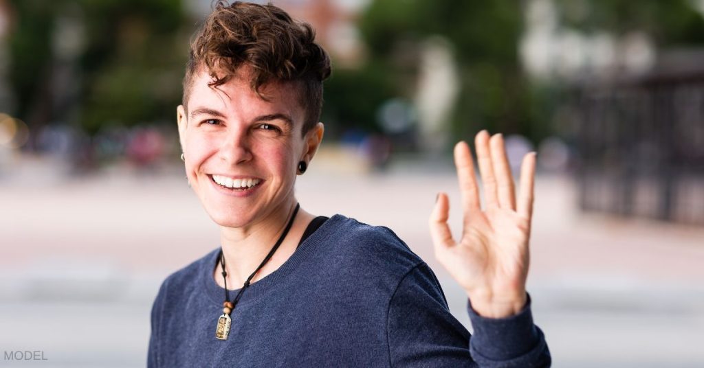 Transgender person smiling and waving. (MODEL)